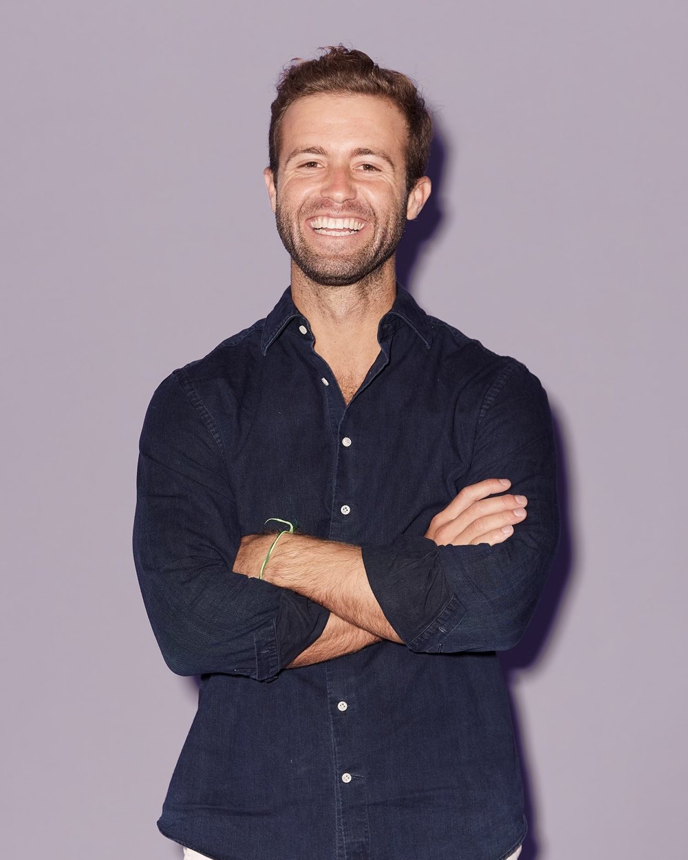 Hunter Johnson, smiling, arms crossed, in a navy shirt against a grey-lilac backdrop